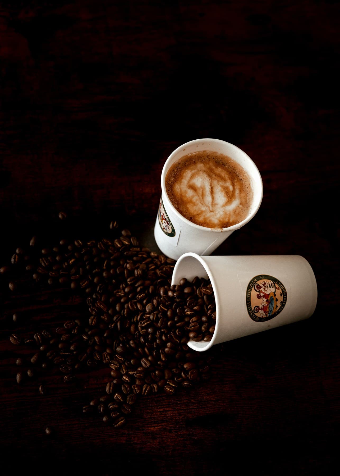 Buna House latte cup and branded coffee cup with roasted beans on a dark wooden table