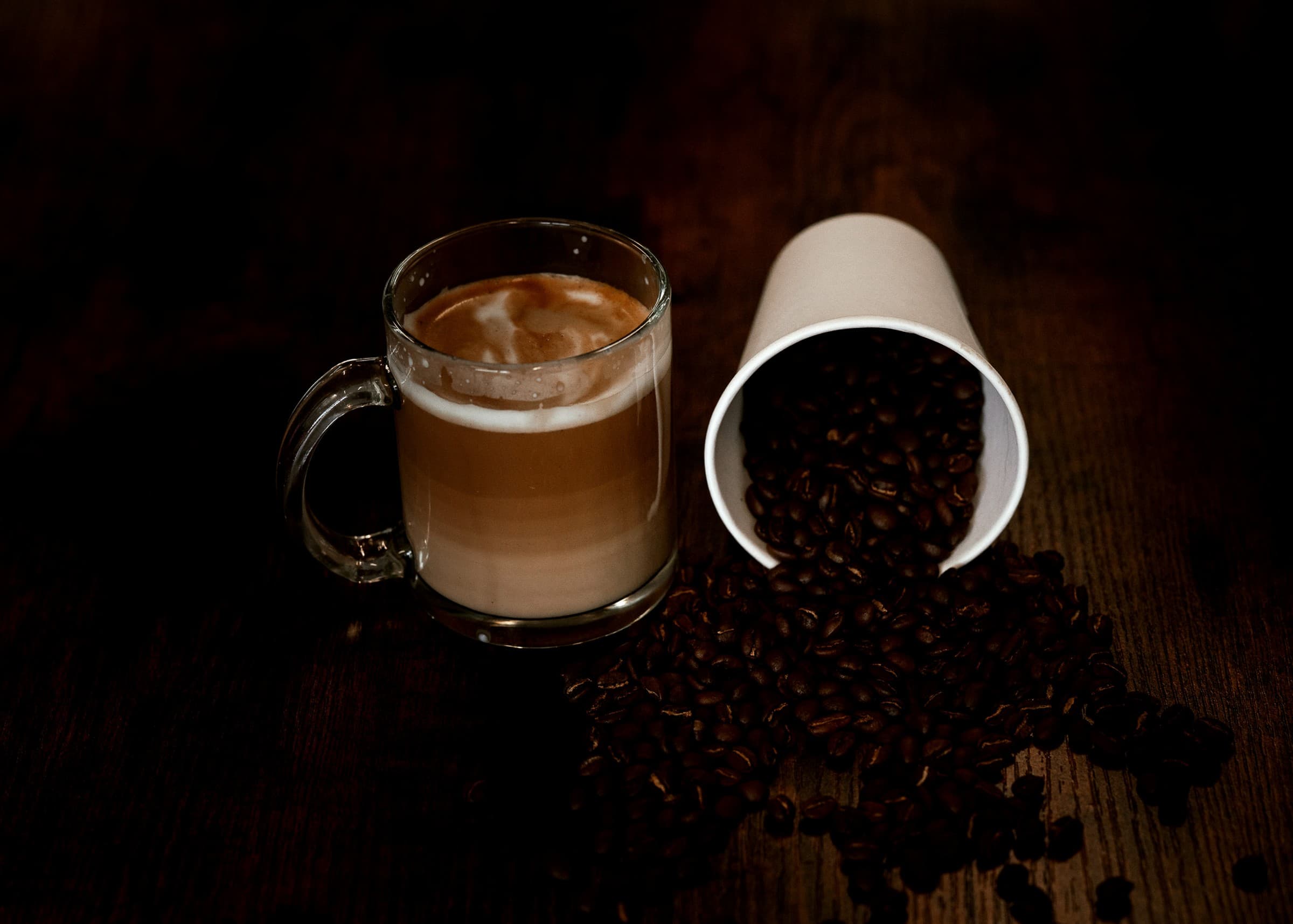 Latte, roasted coffee beans, and Buna House cup arranged on a dark wooden table